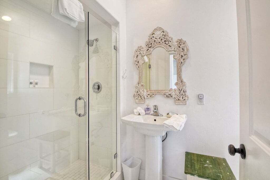 A bathroom with a glass-enclosed shower, a pedestal sink, and an ornate mirror.