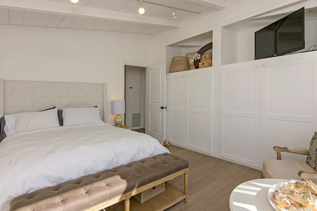 A bedroom with a large bed, a bench, a TV, and a chair.