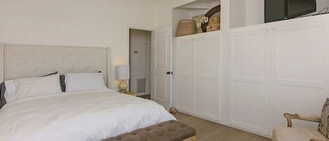 A bedroom with a large bed, a bench, a TV, and a chair.