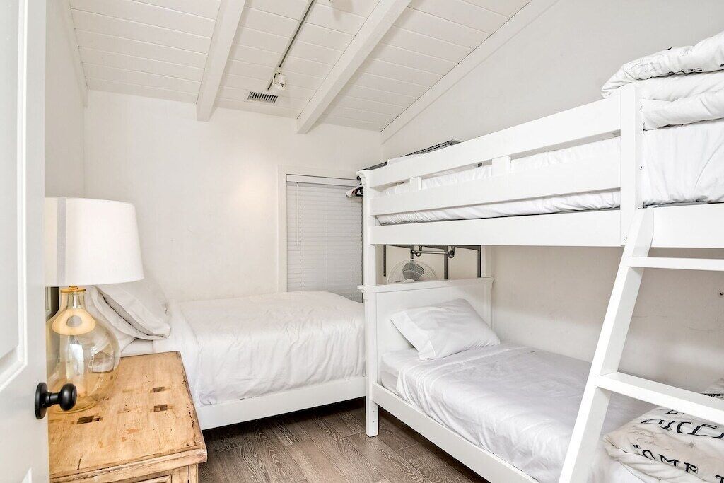 A room with bunk beds, a small wooden table with a lamp, and a window with blinds.