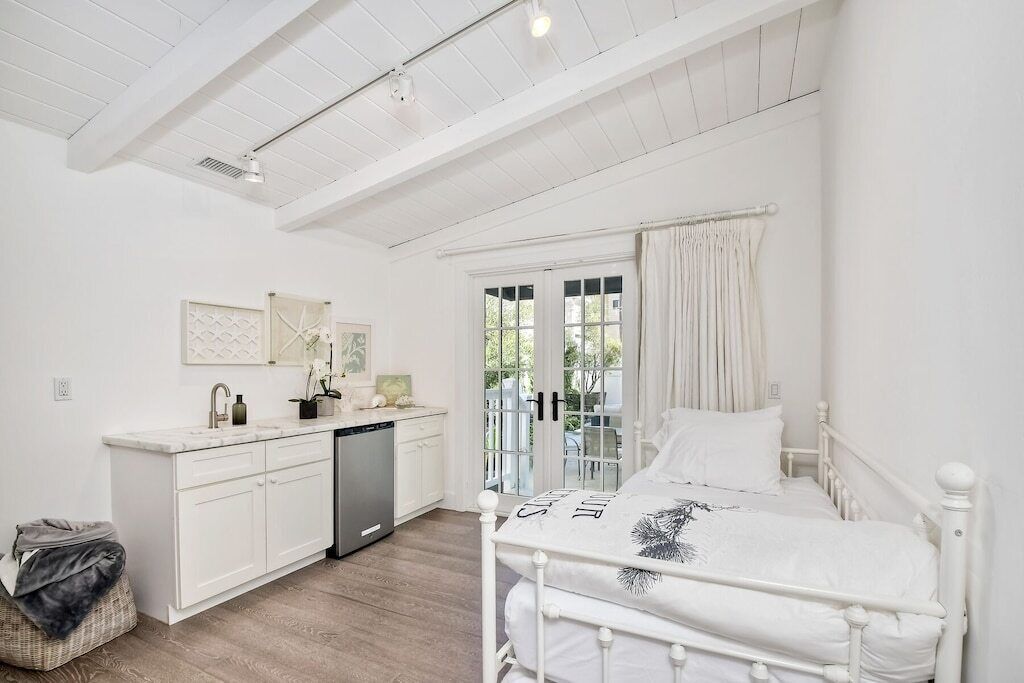 A bedroom with a bed, a bedside table, a window with curtains, and a view of the outdoors.