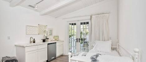 A bedroom with a bed, a bedside table, a window with curtains, and a view of the outdoors.