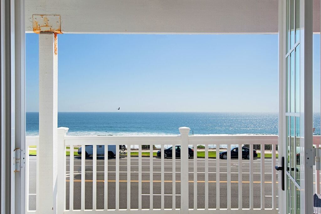 Un balcon avec vue sur l’océan et les voitures garées.