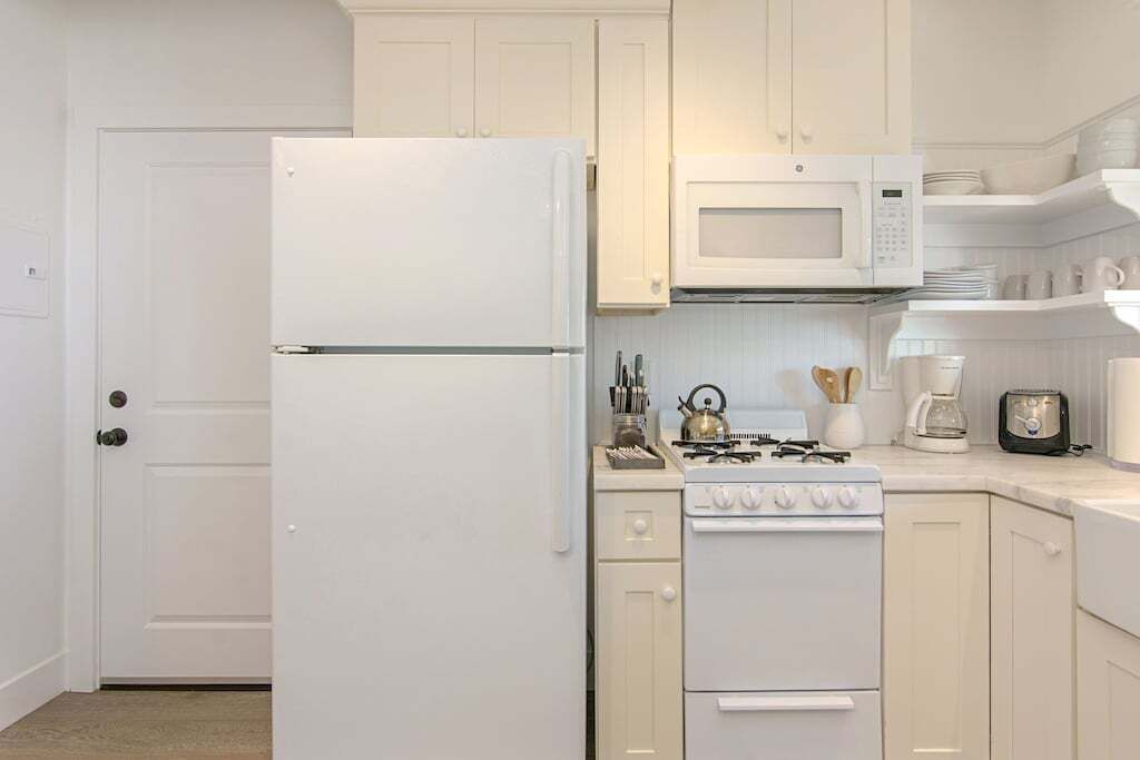 A kitchen with white cabinetry, a refrigerator, a microwave, a stove, and a coffee maker.