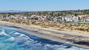 A coastal residential area with houses along the beach, a clear sky, and waves crashing onto the shore. - Ocean View From Private Patio | Across From Beach (Carlsbad)
