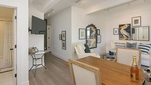 Un salon spacieux avec une table à manger en bois, un ensemble de canapés blancs et un grand miroir.