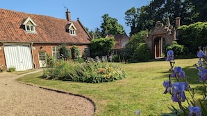 A brick house with a red-tiled roof, a white garage door, and a garden with flowers and shrubs.
