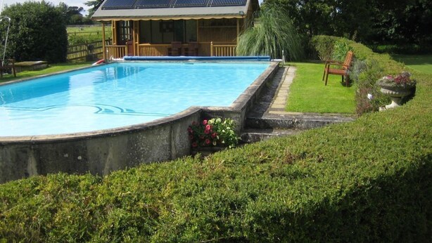 A swimming pool with a wooden deck and a building with solar panels in the background.