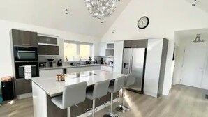 A modern kitchen with a central island, bar stools, stainless steel appliances, and a chandelier. - Luxury Villa Near Ben Nevis, Scottish Highlands (Spean Bridge)