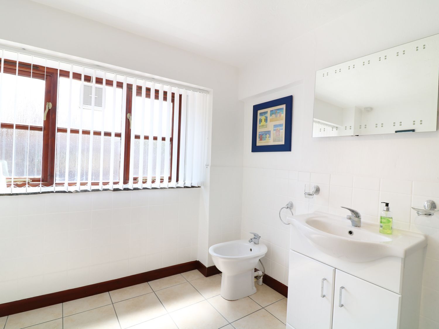A bathroom with a toilet, bidet, sink, and a window with blinds.