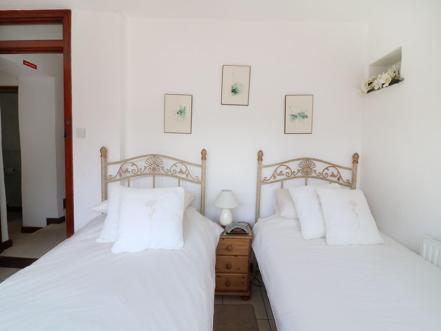 A double room with two beds, a nightstand, and wall-mounted artwork.