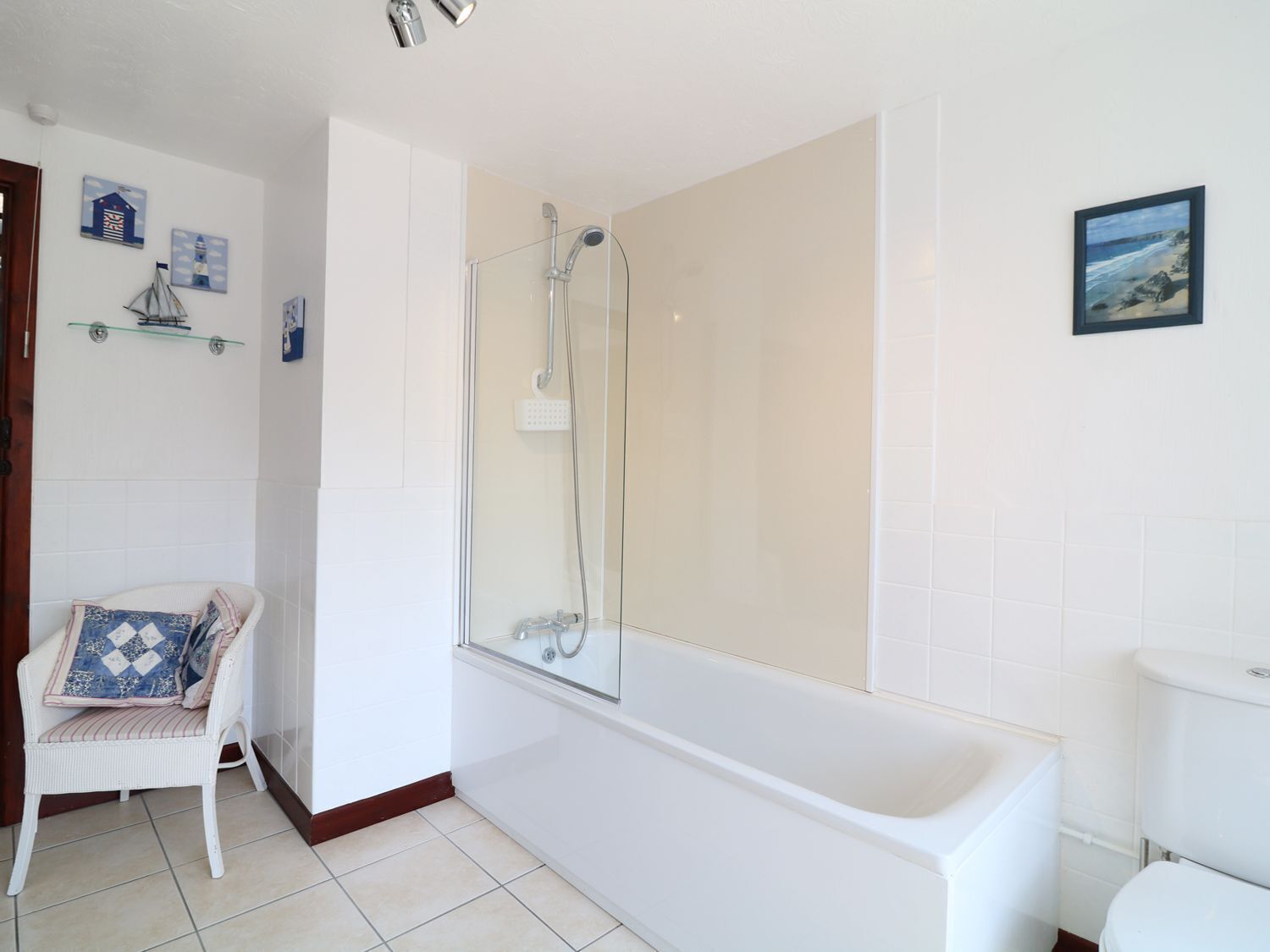 A bathroom with a white bathtub, a glass-enclosed shower, a white toilet, and a chair with a patterned cushion.