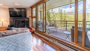 Un salon confortable avec une cheminée, un grand téléviseur et un balcon agrémenté de meubles d’extérieur.