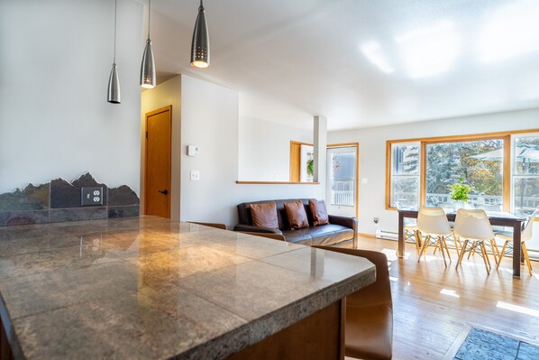 A modern kitchen with a large island, a dining area with a wooden table and chairs, and a seating area with a sofa and cushions.