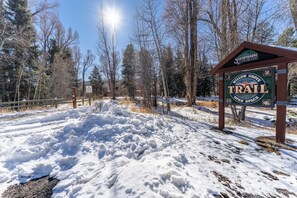 A snow-covered trail sign with a wooden structure and trees in the background.