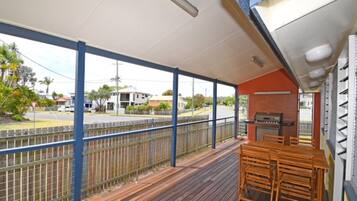 Ein überdachter Außenbereich mit Holzdeck, Grill und Tisch mit Stühlen.