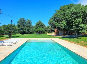 A rectangular swimming pool with clear blue water, surrounded by a paved deck.