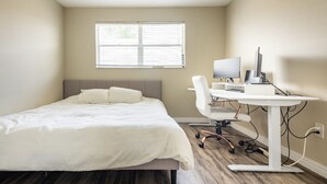 Une chambre avec un lit, un bureau avec un ordinateur et une fenêtre.