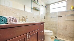 Une salle de bain avec un mur en marbre, un lavabo avec un miroir, des toilettes et un espace douche.