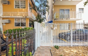 A gated residential area with a parked car, a white gate, and a yellow building with balconies.