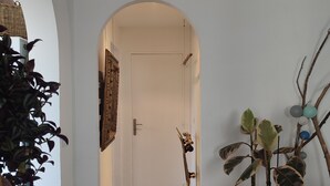Een gang met een witte deur, een houten bankje en een plant in pot.