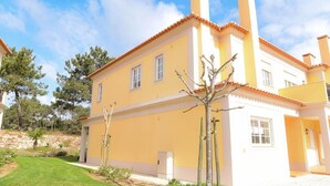 A two-story yellow building with a tiled roof, a small garden, and a clear sky. - Burgo D. Sebastião 27B (Óbidos)
