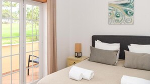 A hotel room with a bed, pillows, a nightstand, a lamp, and a view of a garden through a sliding door. - Burgo D. Sebastião 27B (Óbidos)