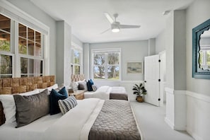 A bedroom with two beds, a ceiling fan, and large windows.