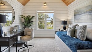 A bedroom with a wooden ceiling, a desk with a chair, a bed with blue bedding, a window with a view, and a painting on the wall. - Large Peaceful Home | Hot Tub, Dock Near Beach (Savannah)