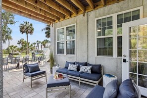 An outdoor patio area with a wooden ceiling, a sofa set, and a dining table with chairs.