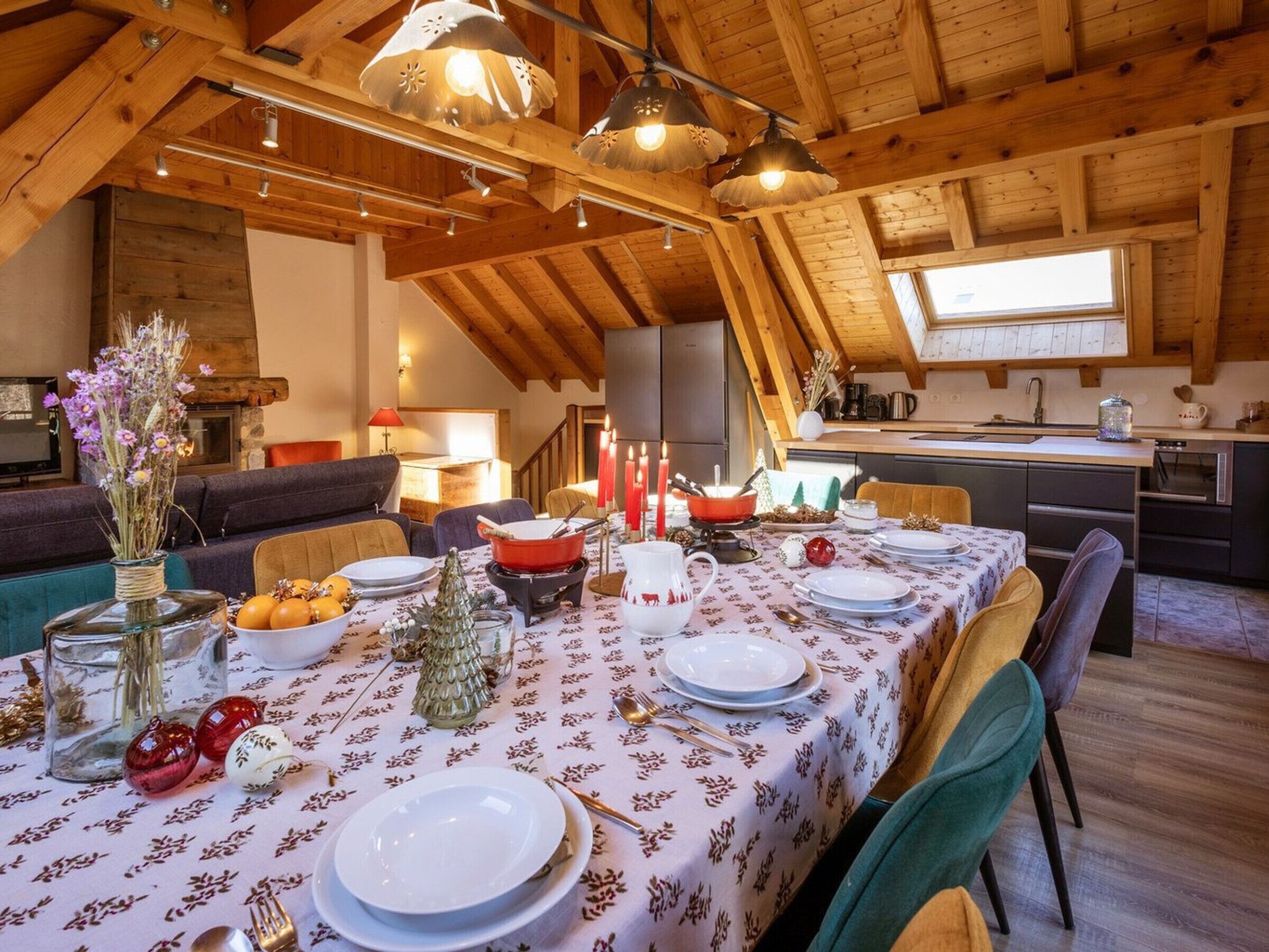 Un comedor con una mesa dispuesta para cuatro personas, vigas de madera en el techo y una cocina al fondo.