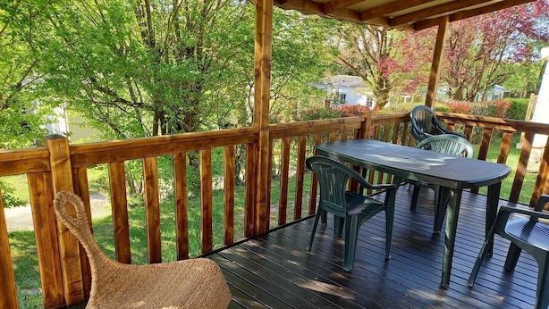 Una terraza de madera con una mesa y sillas, rodeada por una barandilla de madera y abundante vegetación.