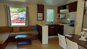 Un espacio habitable compacto con sofá, una pequeña mesa de comedor, kitchenette y una ventana con persianas.