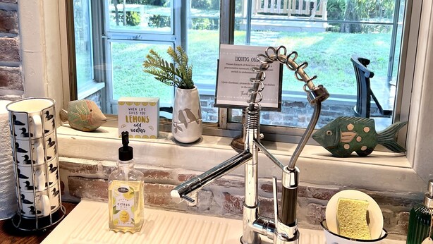 A bathroom with a window, a sink, a faucet, and a small shelf with a bottle of hand soap and a decorative fish. - Dreamy River Cottage (Inverness)
