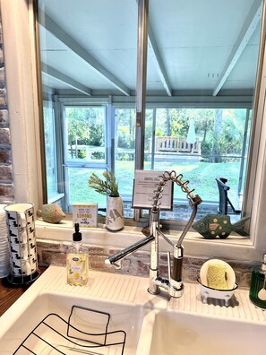Un baño con ventana, un lavabo, un grifo y un pequeño estante con una botella de jabón para manos y un pez decorativo.