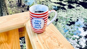 A wooden deck with a mug that reads "YOU ONLY LIVE ONCE" overlooking a river surrounded by trees. - Dreamy River Cottage (Inverness)