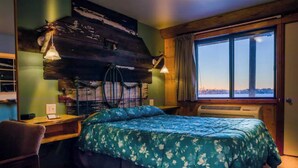 A room with a bed, a desk, a chair, a window with a view, and a wall with a rustic design. - Quaint room overlooking the lake called   Hummingbird Haven - Curriers Lakeview (Rice Lake)