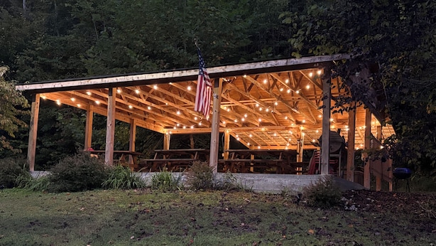 Un padiglione in legno con luci a tendina e una bandiera americana, immerso nel verde.