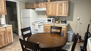 Una cucina compatta con mobili in legno, un frigorifero bianco, un forno a microonde, un piano cottura e un tavolo da pranzo con sedie.