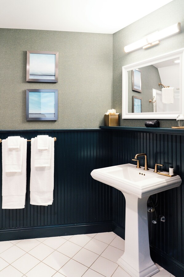 A bathroom with a white pedestal sink, dark wood paneling, and two framed pictures on the wall.