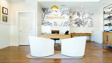 A modern office space with a desk, two white chairs, a wooden desk, a hanging pendant light, and a wall with a floral pattern.