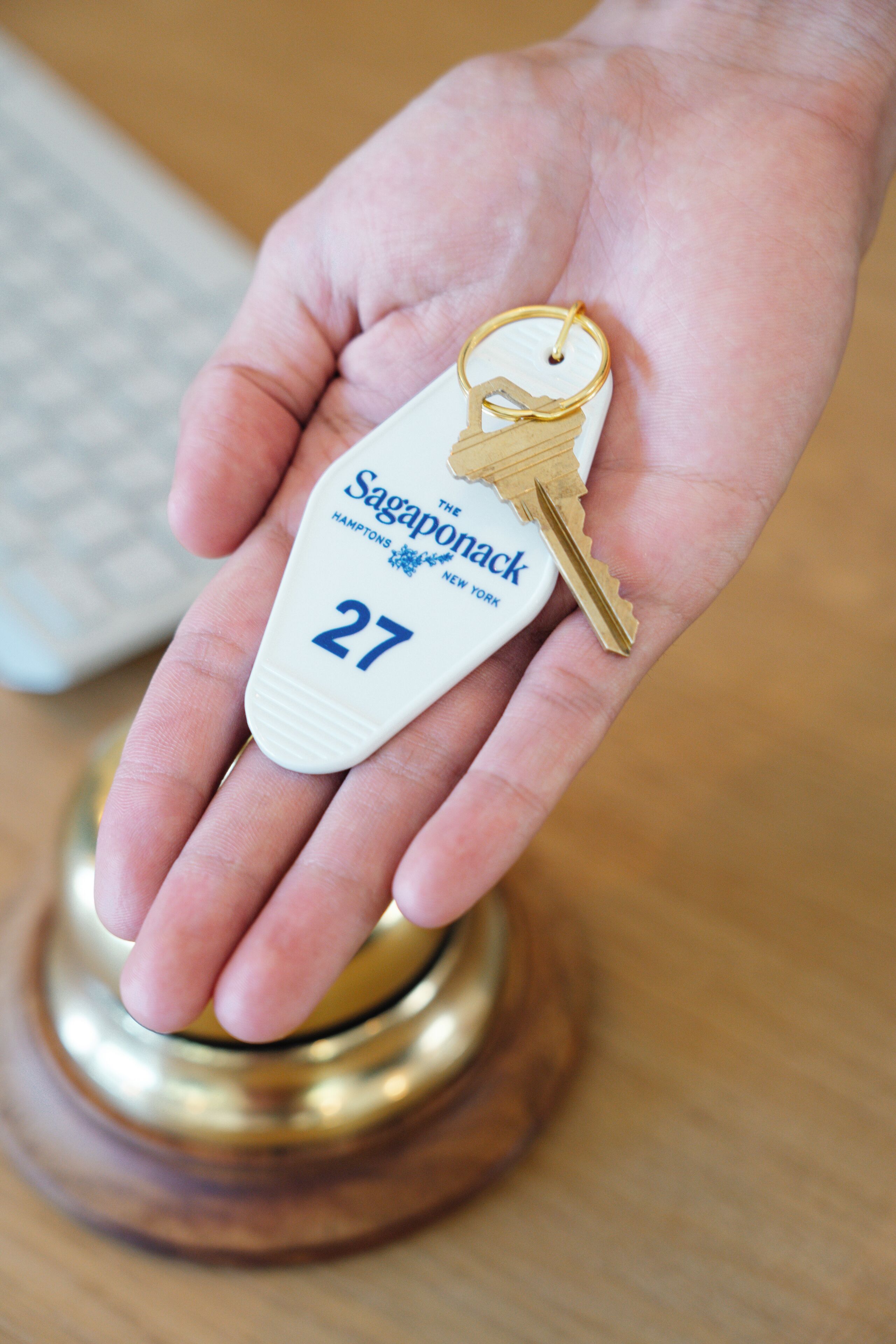 A hand holding a key with a tag labeled "Saginaponack Hamptonton, New York 27".