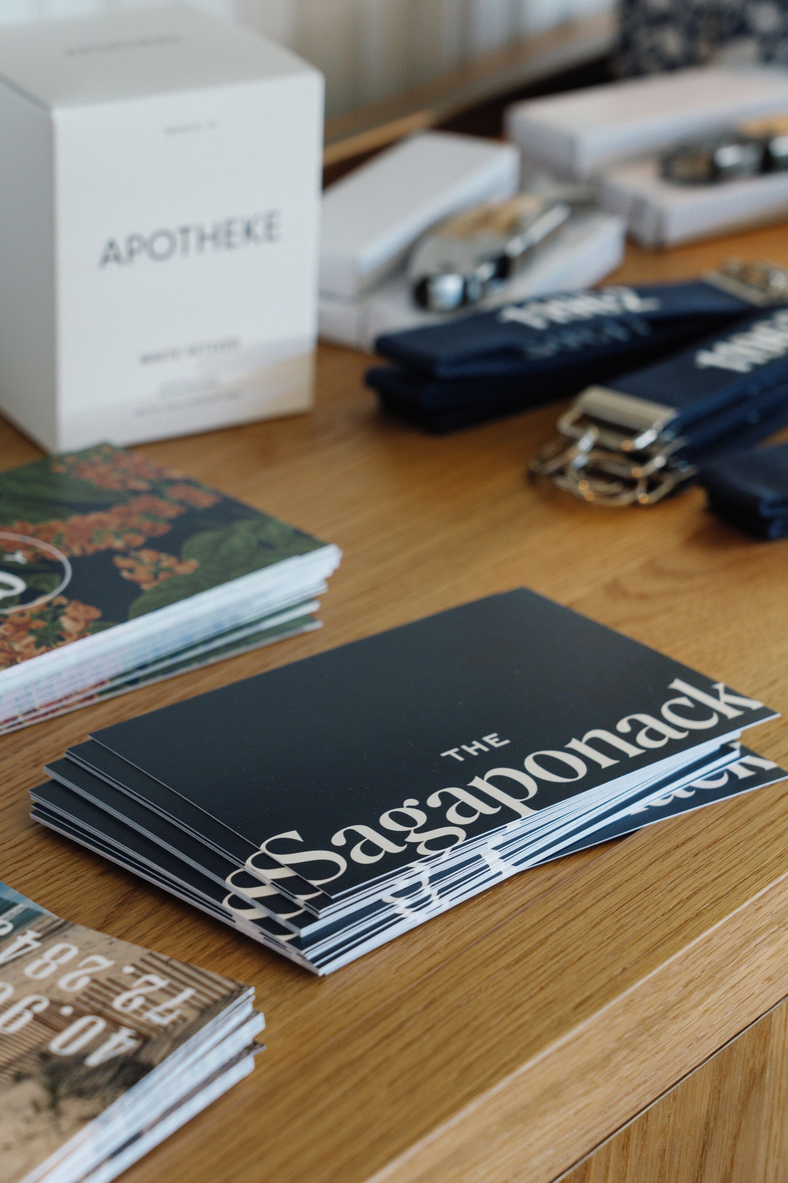 A wooden table with a stack of magazines, a white box labeled 'APOTHEKE', and some folded clothing.