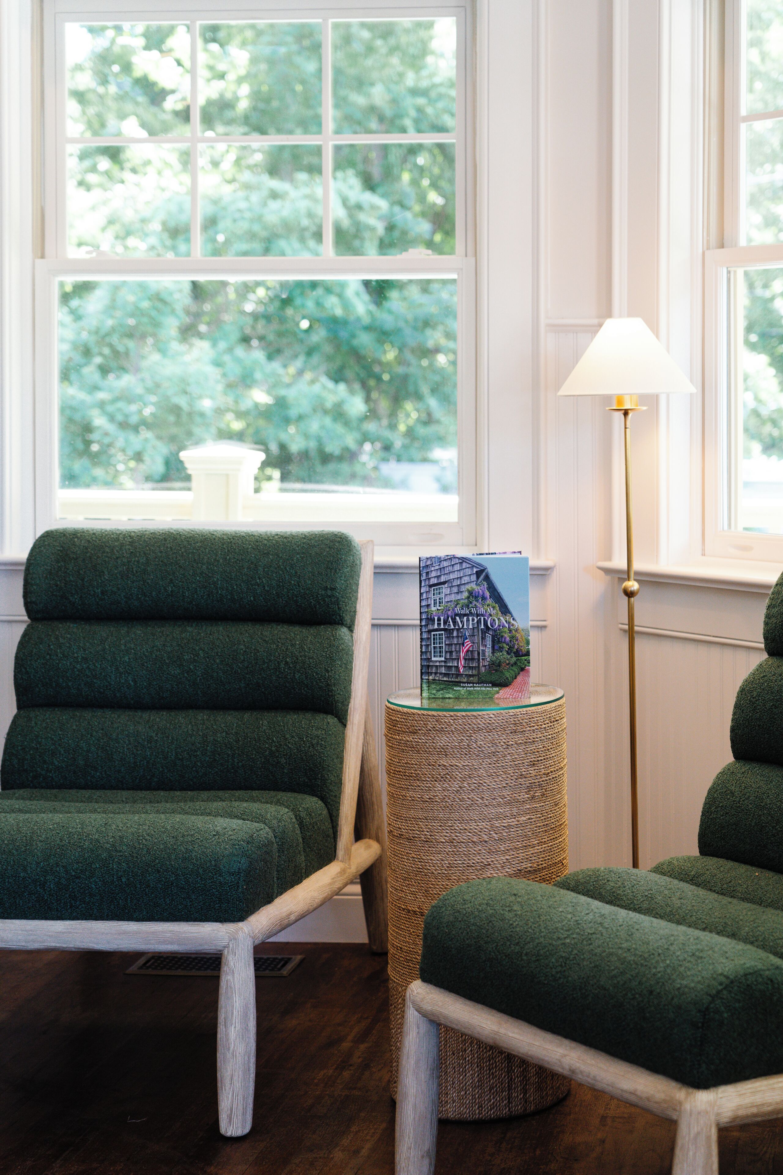 A room with a green upholstered chair, a small round table with a book, and a floor lamp.