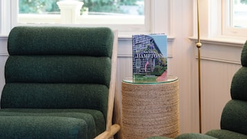 A room with a green upholstered chair, a small round table with a book, and a floor lamp.