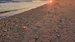 Une plage de galets et de sable, un coucher de soleil et une mer calme.