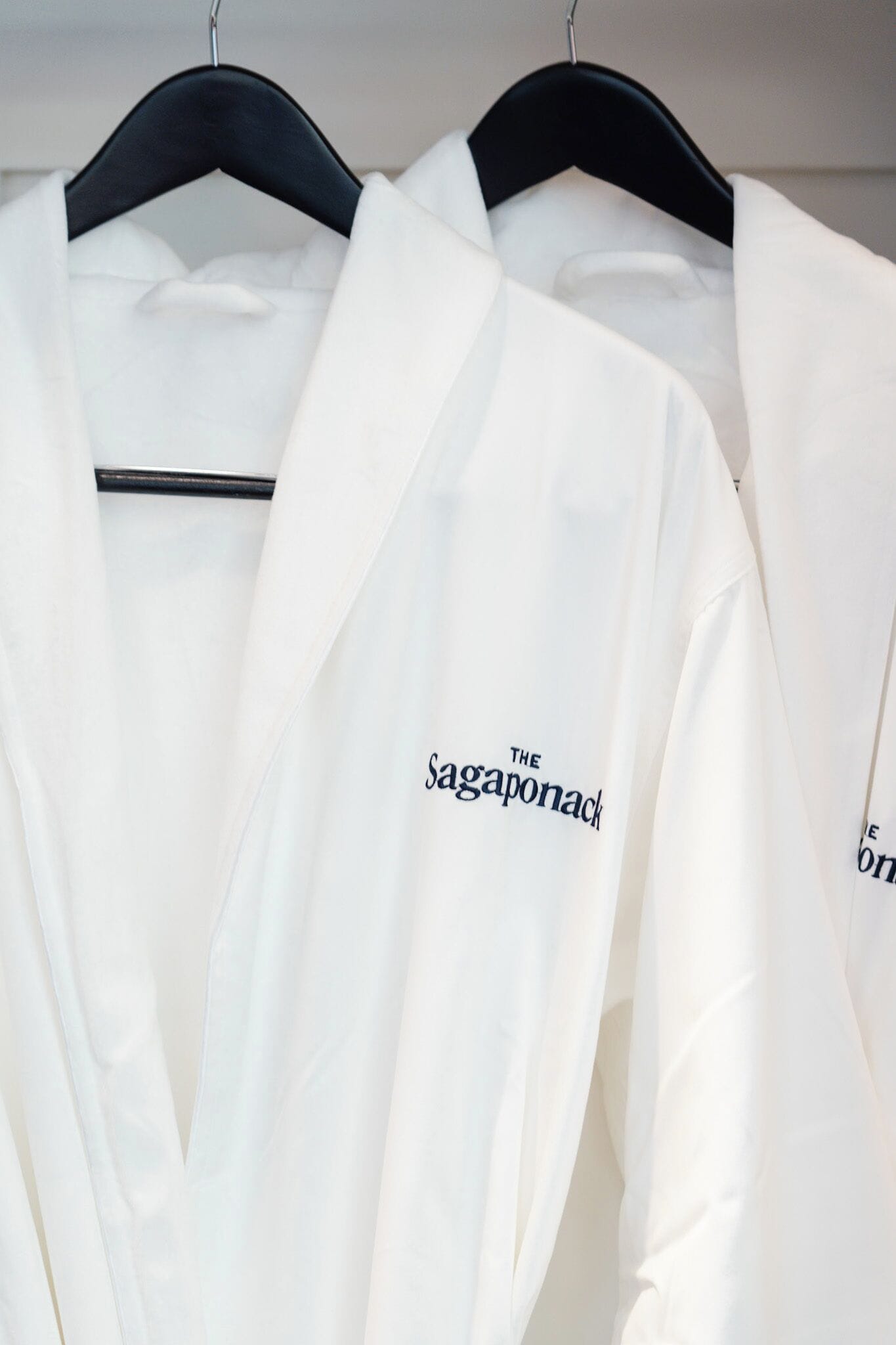 Two white robes hanging on a black hanger.