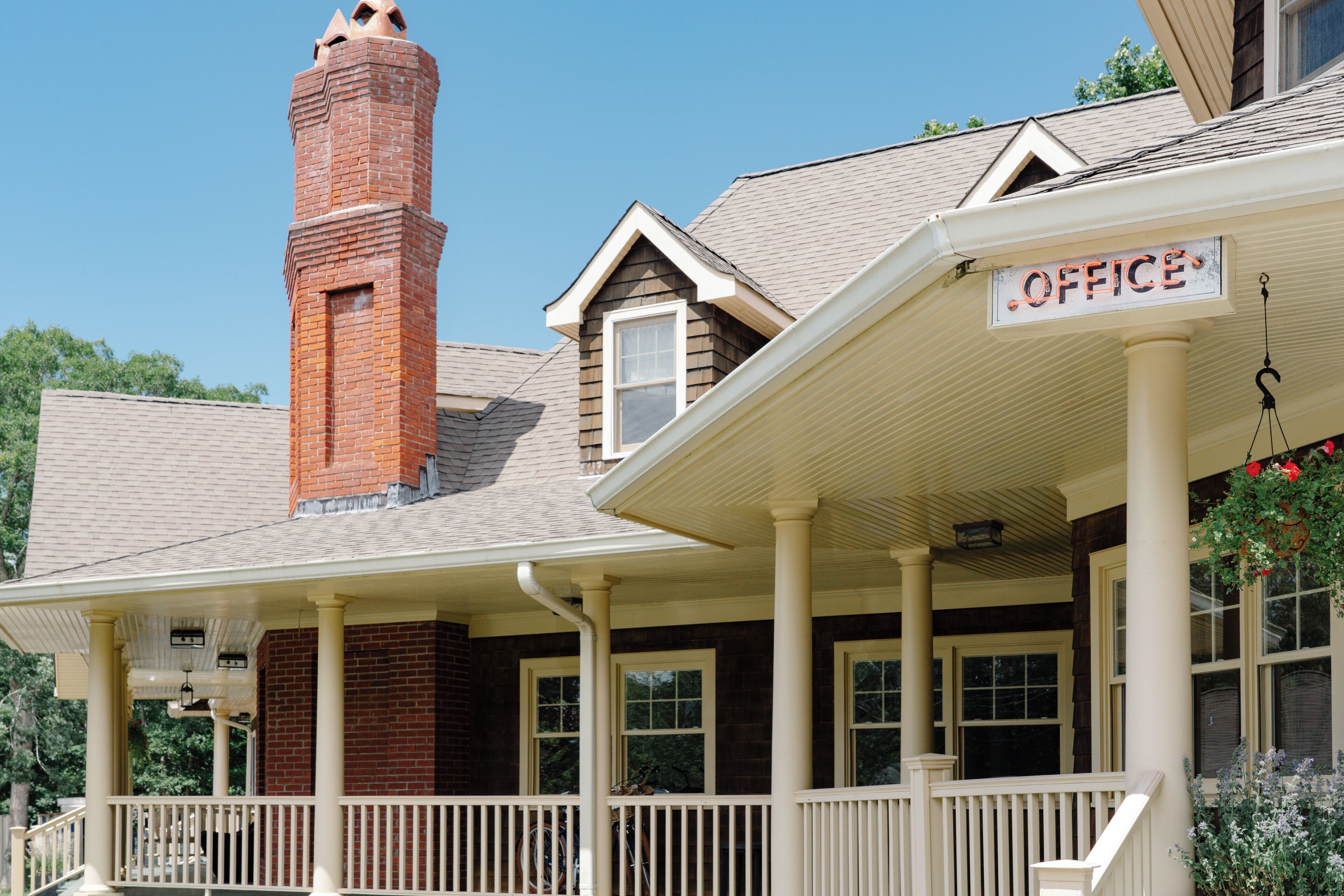 A building with a brick chimney, a porch with white railings, and a sign that reads "OFFICE".