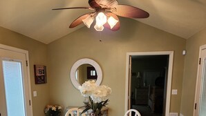 Un comedor con una mesa de vidrio, sillas blancas, un ventilador de techo y un espejo en la pared.