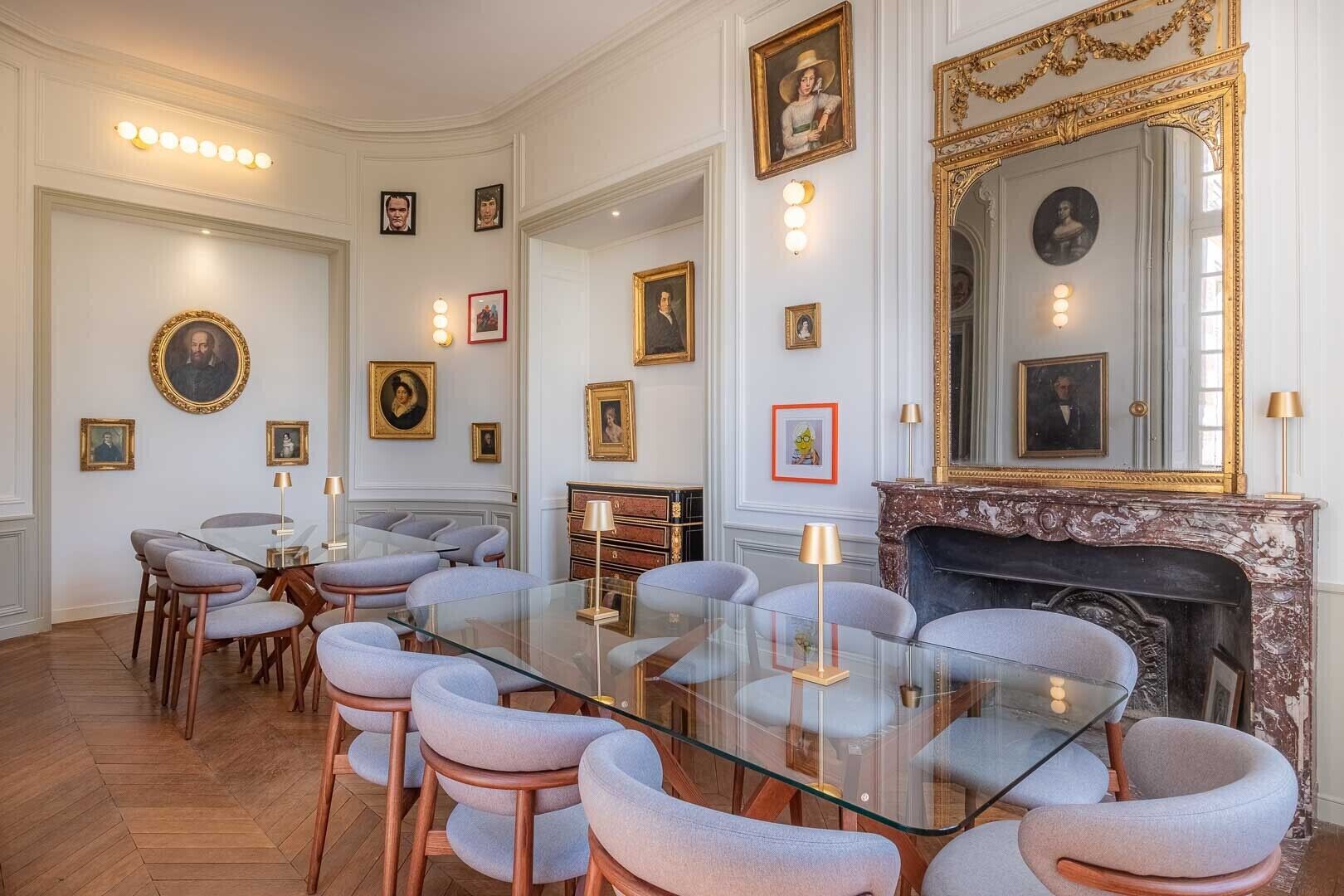 A formal dining room with a glass table, cushioned chairs, and a fireplace.